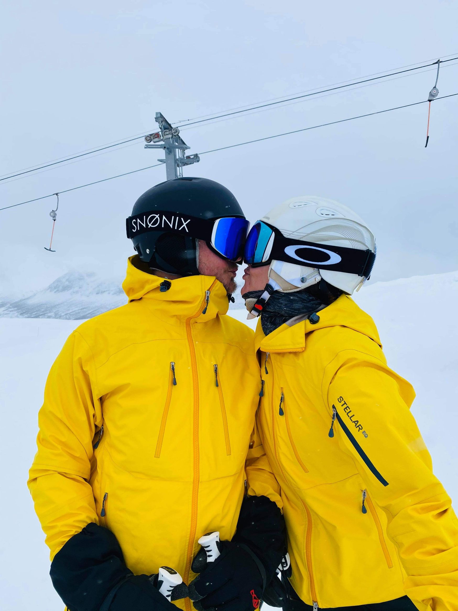 To personer i gule skidresser og utstyr kysser