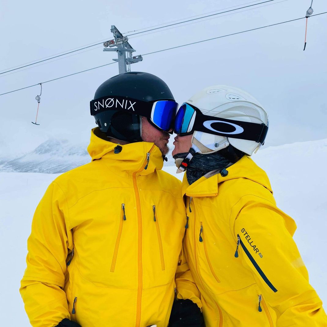 To personer i gule skidresser og utstyr kysser