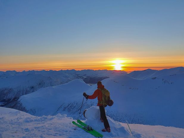 Person på ski ser utover fjellene i solnedgang