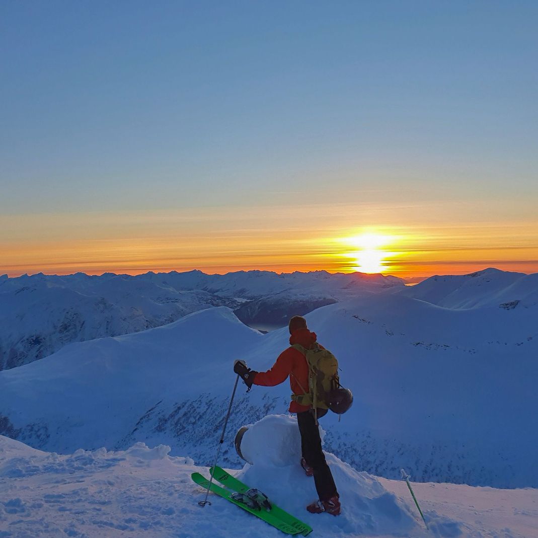 Person på ski ser utover fjellene i solnedgang