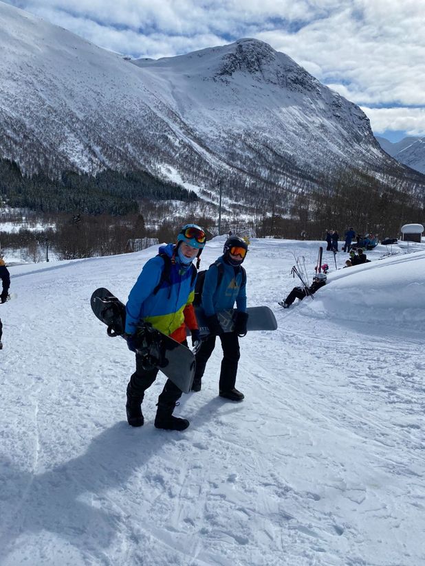 To personer med snowboard under armen går opp bakke