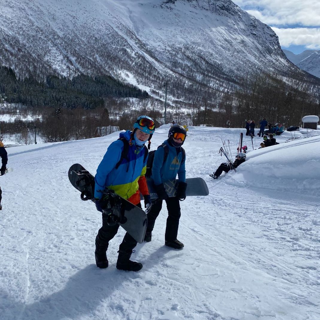 To personer med snowboard under armen går opp bakke